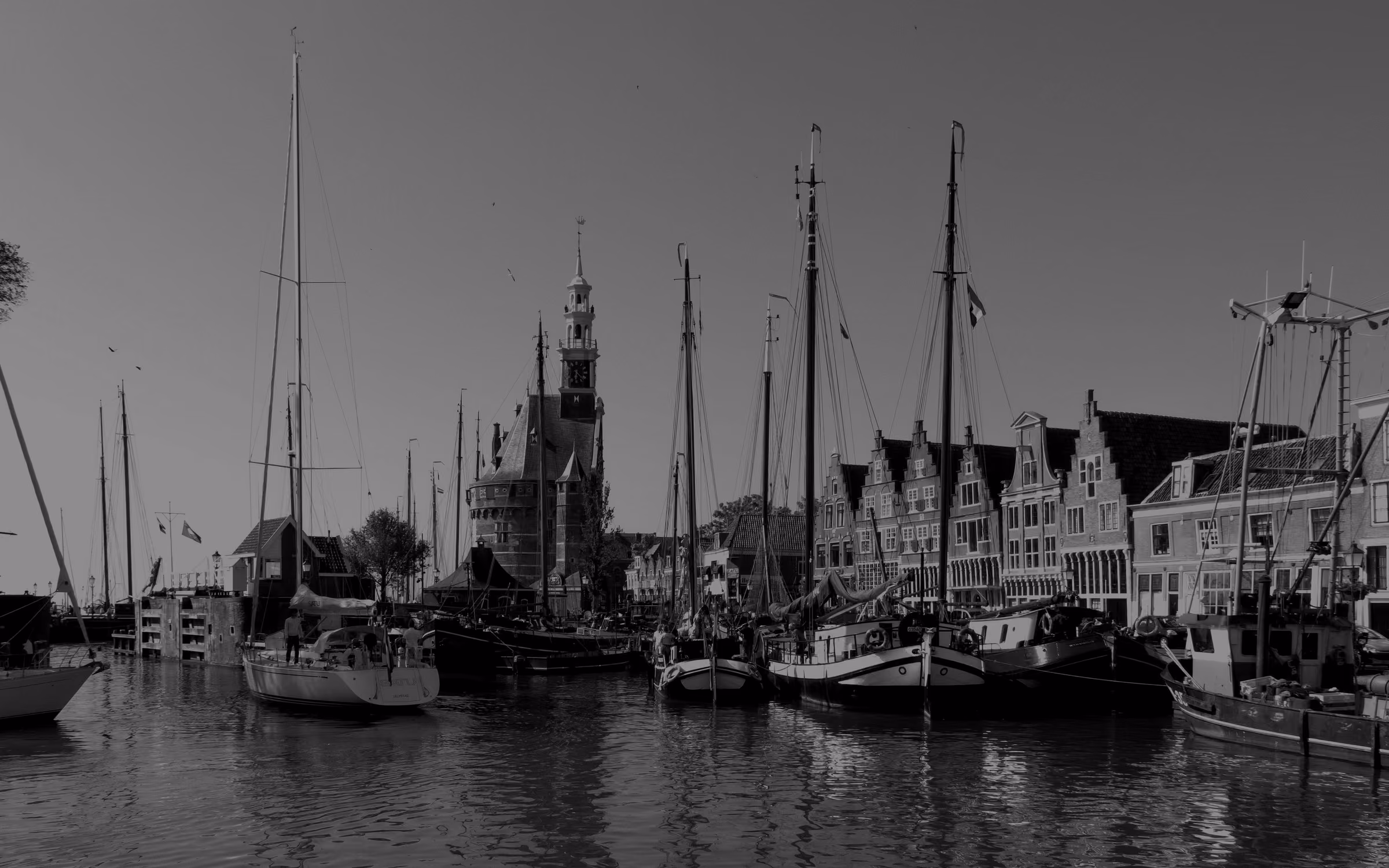 Sailing ships moored in Hoorn's old harbour beneath the Hoofdtoren and a row of gabled houses.