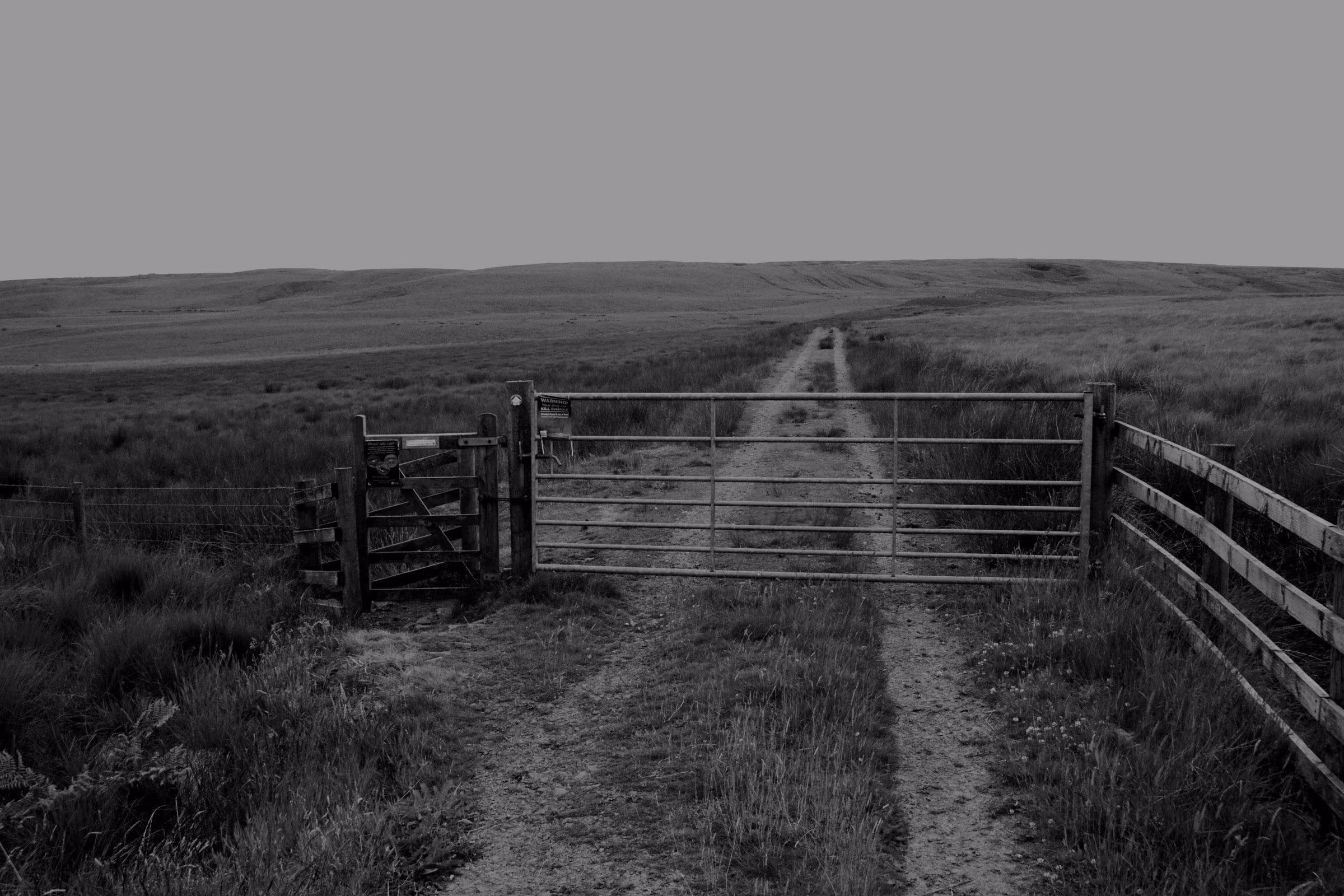 A dirt track leads through a gate into green moorland.