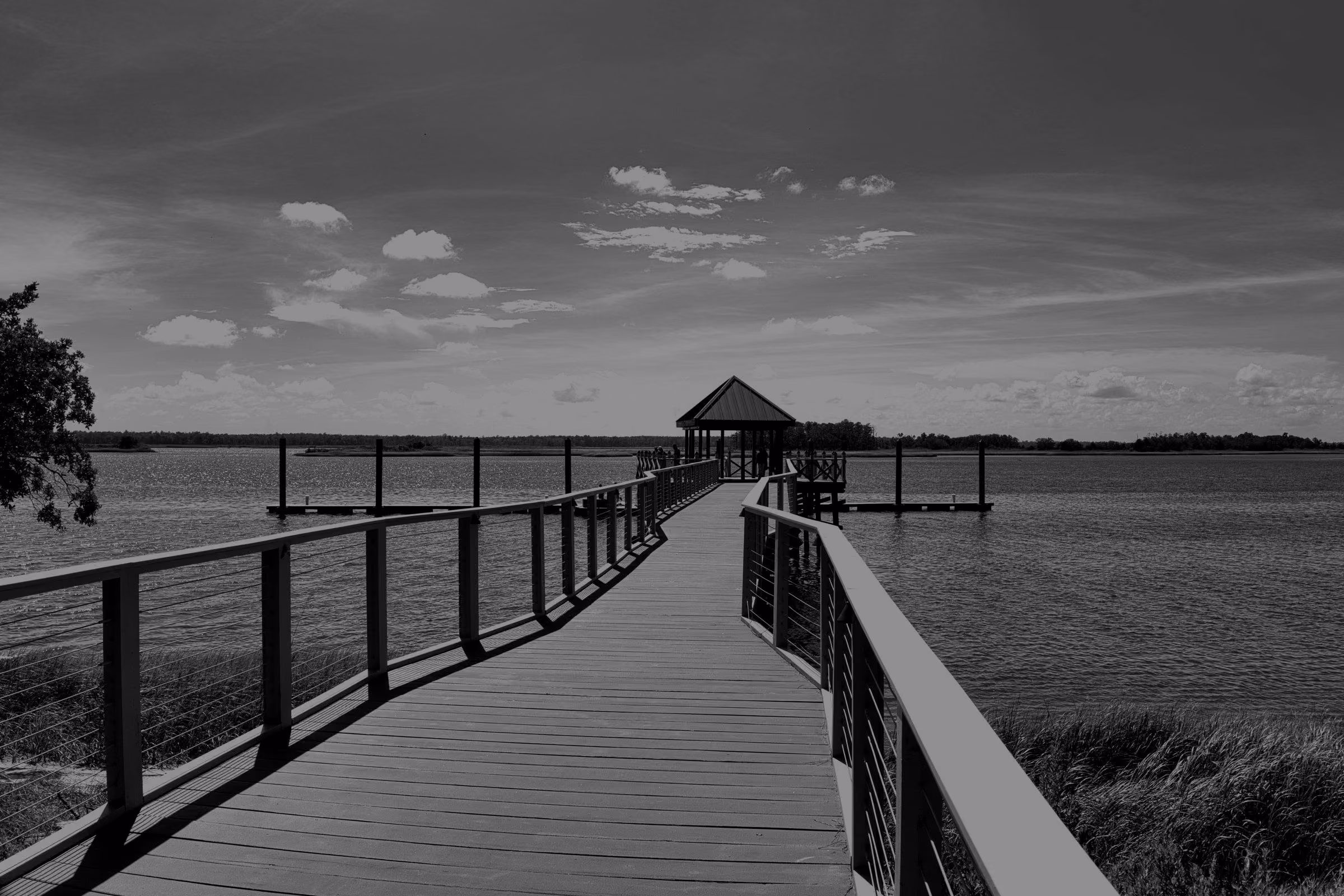 A long wooden pier extends over calm lake water under a blue sky.