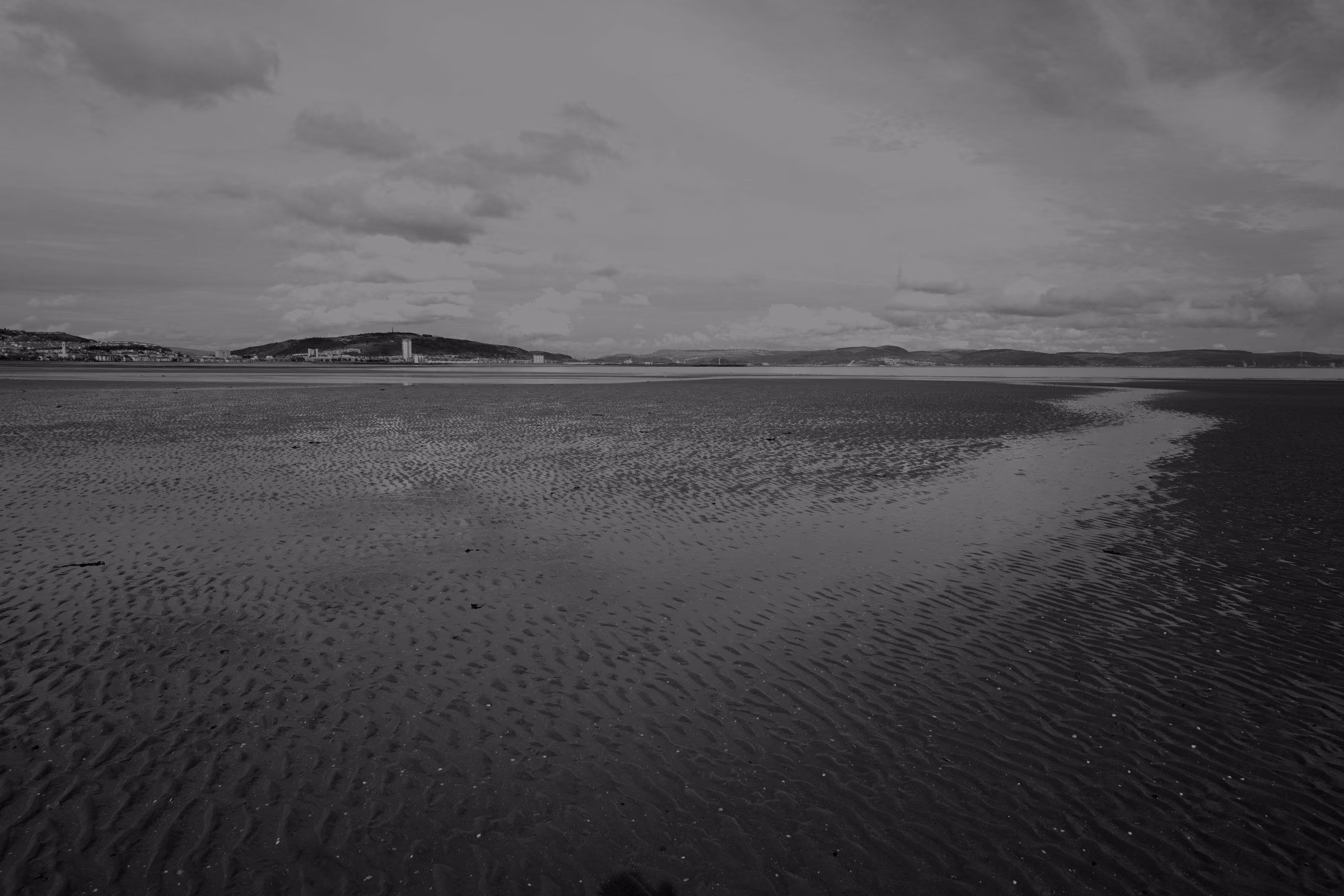 A wide view of Swansea Bay at low tide showing the shoreline and distant hills.
