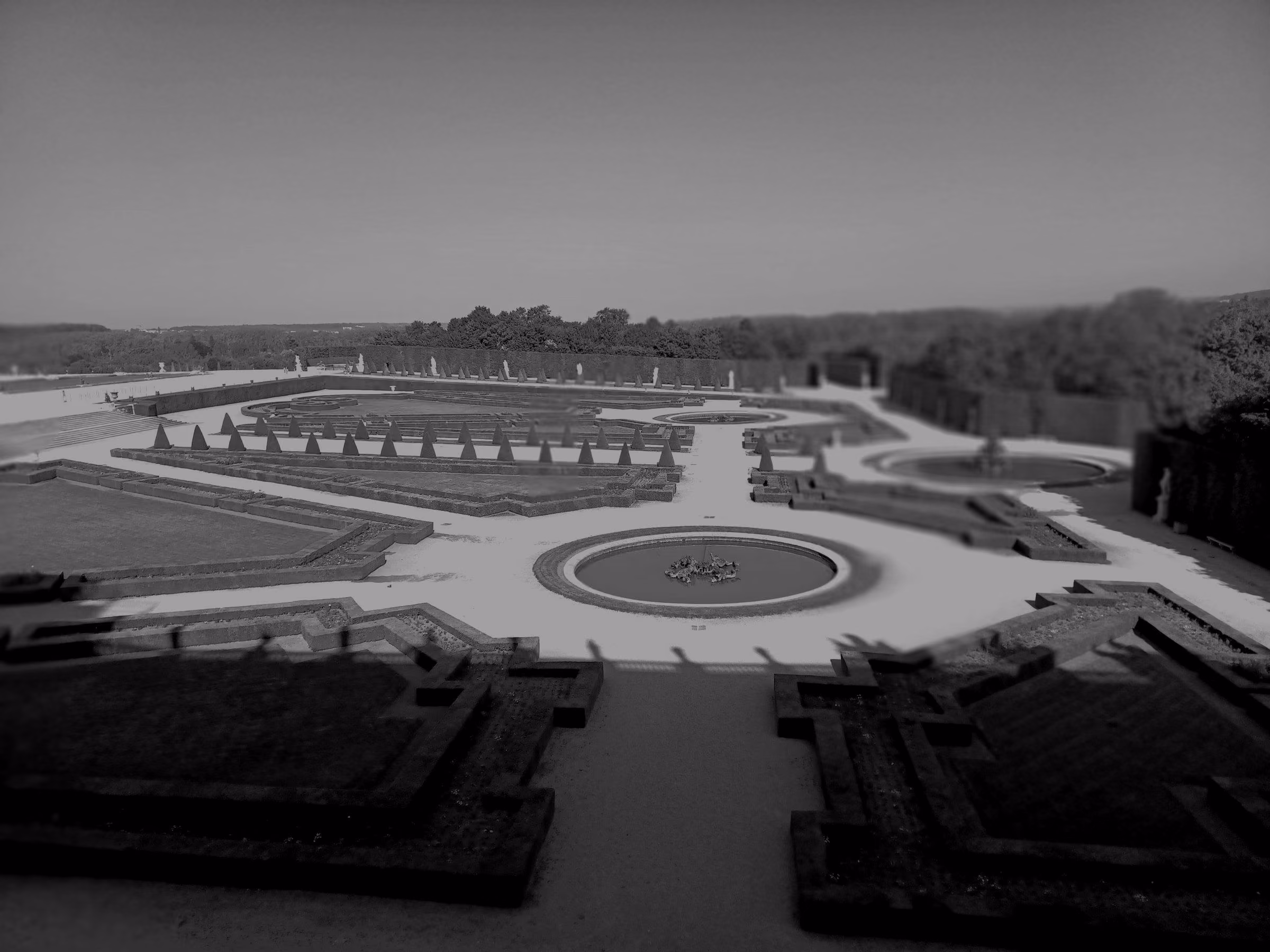 A grand palace surrounded by expansive formal gardens and a large reflecting pool, located in Versailles, France.