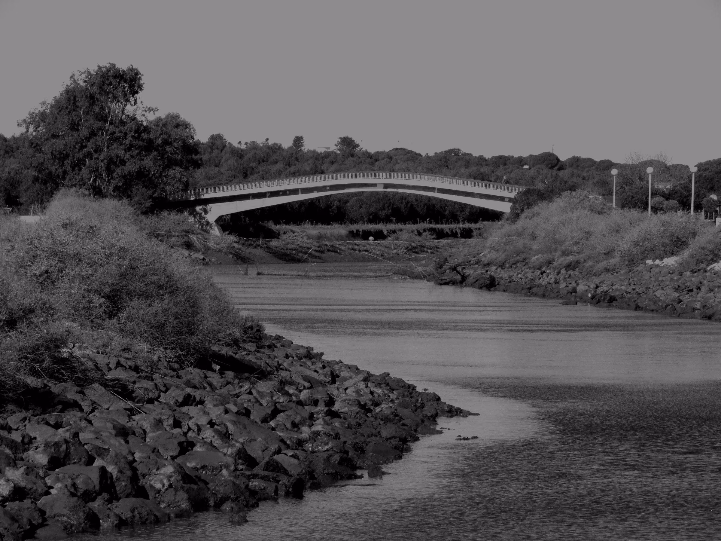 A wide view of the Quarteira river with a footbridge crossing it.