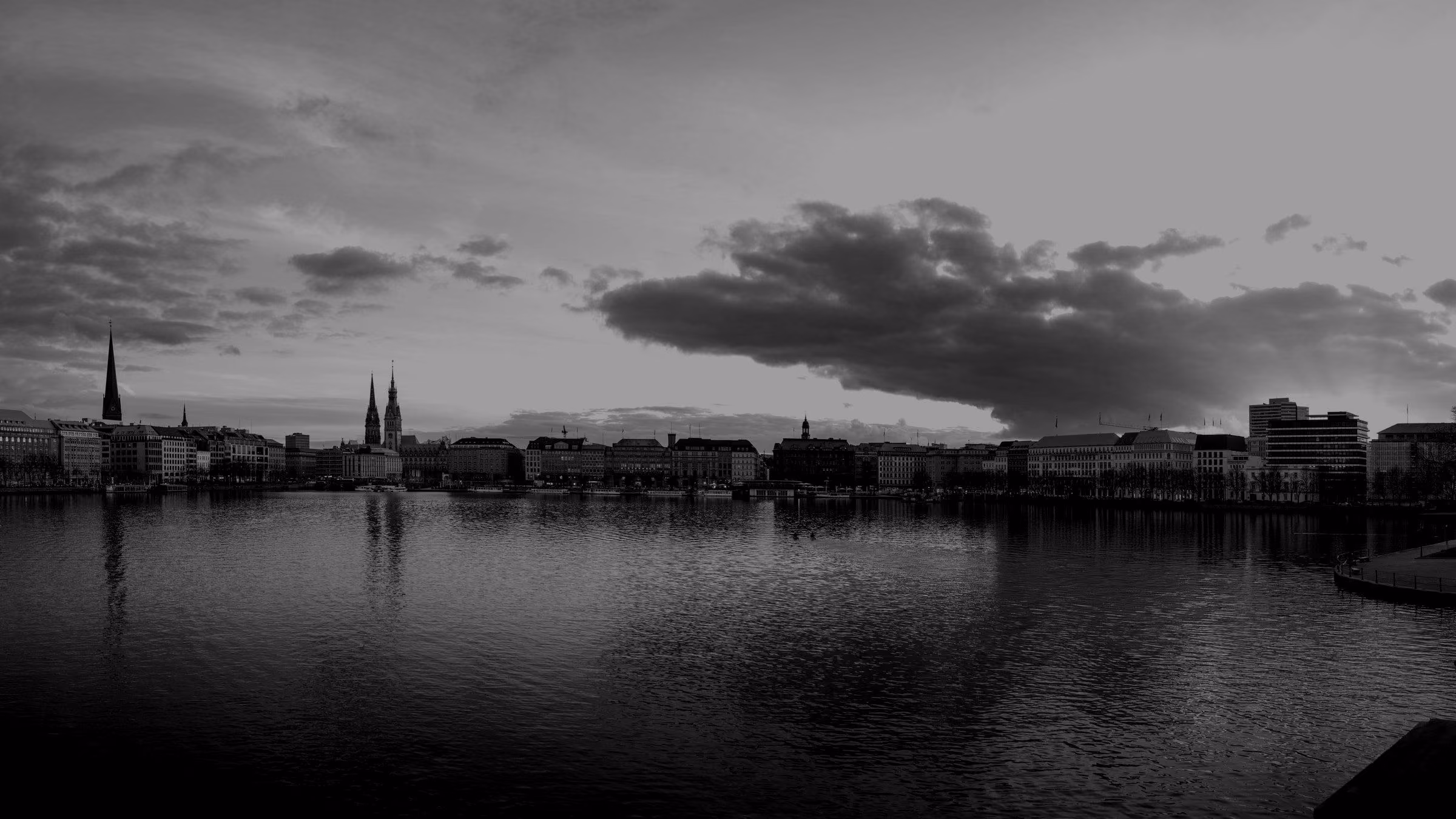 A wide view of the Hamburg skyline reflected in Alster Lake during a sunset.